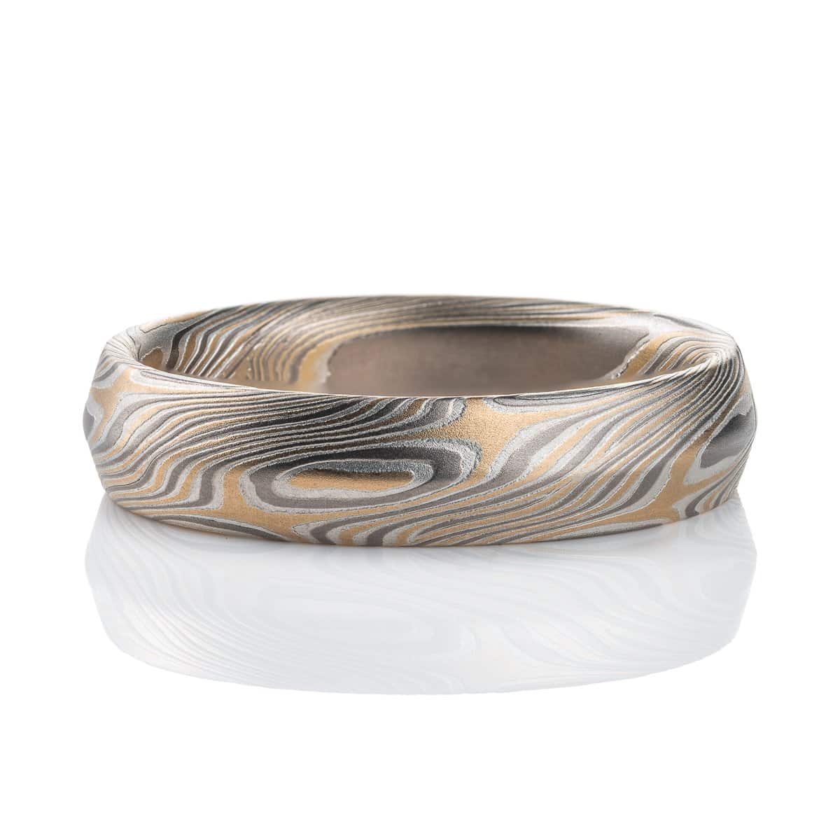 Mokume gane ring with beveled profile, patterned in long swooping lines and starburst like arcs. Made with yellow gold, silver and palladium.