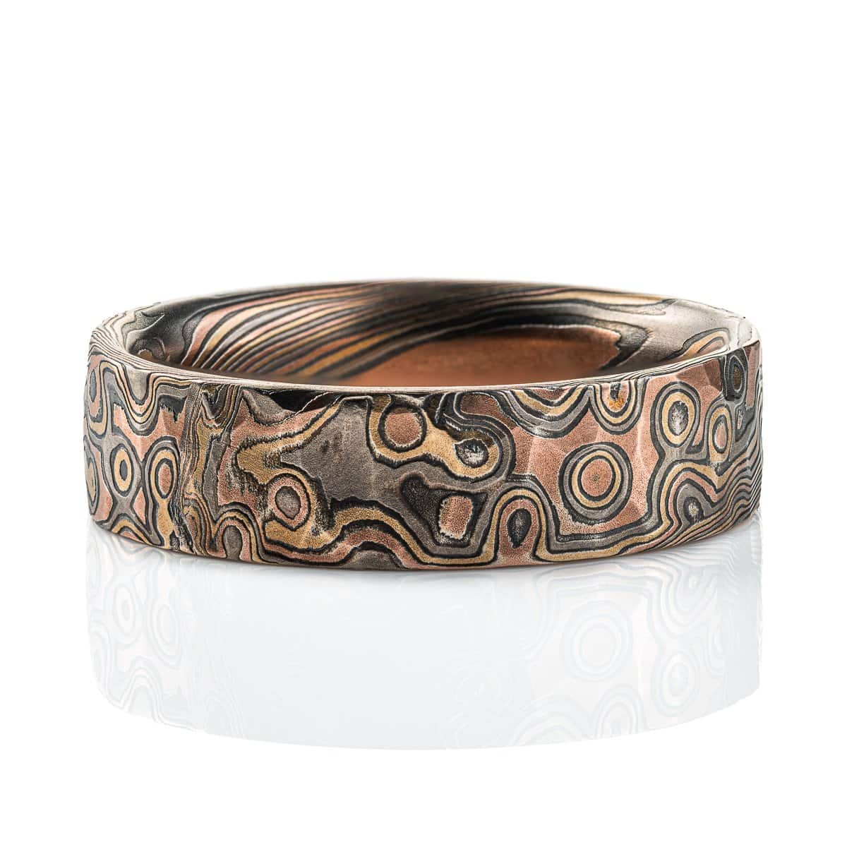 Textured mokume gane ring with flat profile, patterned in a mixture of lines and dots, and made with layers of red gold, yellow gold, palladium and oxidized silver.