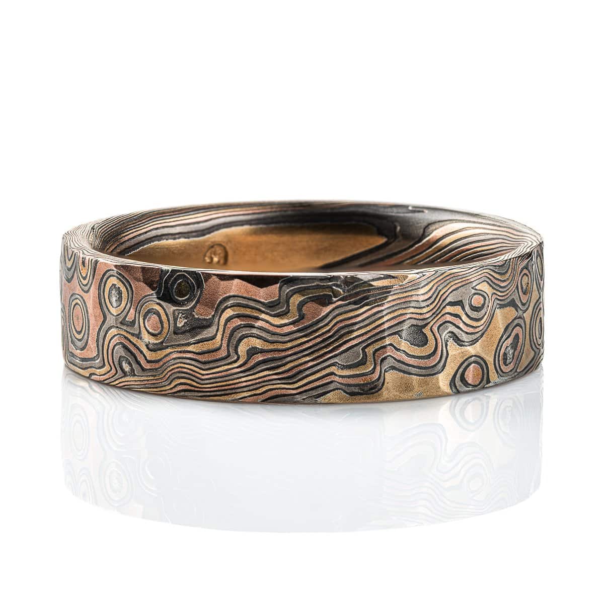 Textured mokume gane ring with flat profile, patterned in a mixture of lines and dots, and made with layers of red gold, yellow gold, palladium and oxidized silver.