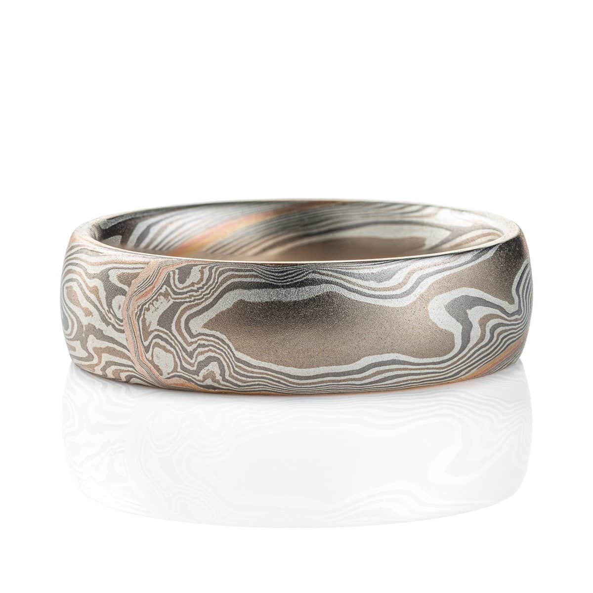 Domed mokume gane band, with a smooth surface, the ring is mainly layers of dark and light gray, with a stripe of red gold and yellow gold at the center. The lines of the pattern run diagonally across and twisting around the ring.