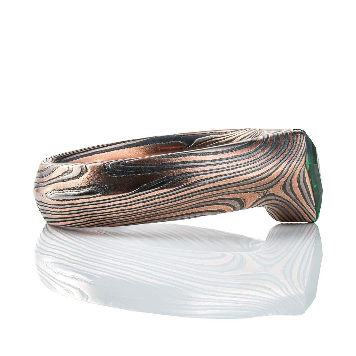 Statement mokume gane ring made with red gold, palladium and oxidized silver, with a bright green kite shaped stone, the band wraps around the long point of the stone.
