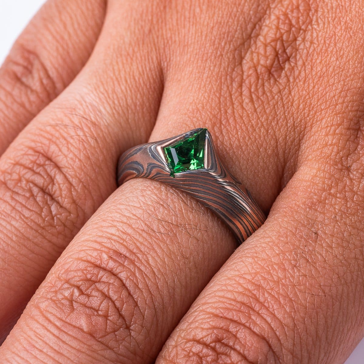 Statement mokume gane ring made with red gold, palladium and oxidized silver, with a bright green kite shaped stone, the band wraps around the long point of the stone.