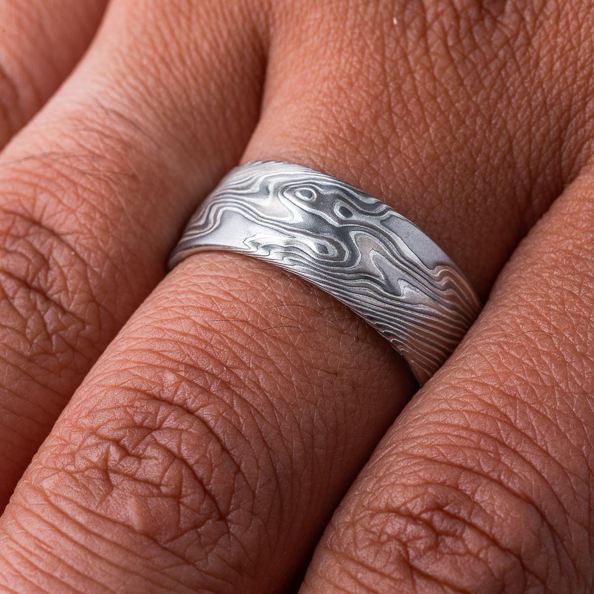 Wide men's mokume gane ring, etched for texture, and carved on the surface to add subtle ripples and waves. Made with palladium, silver and white gold.
