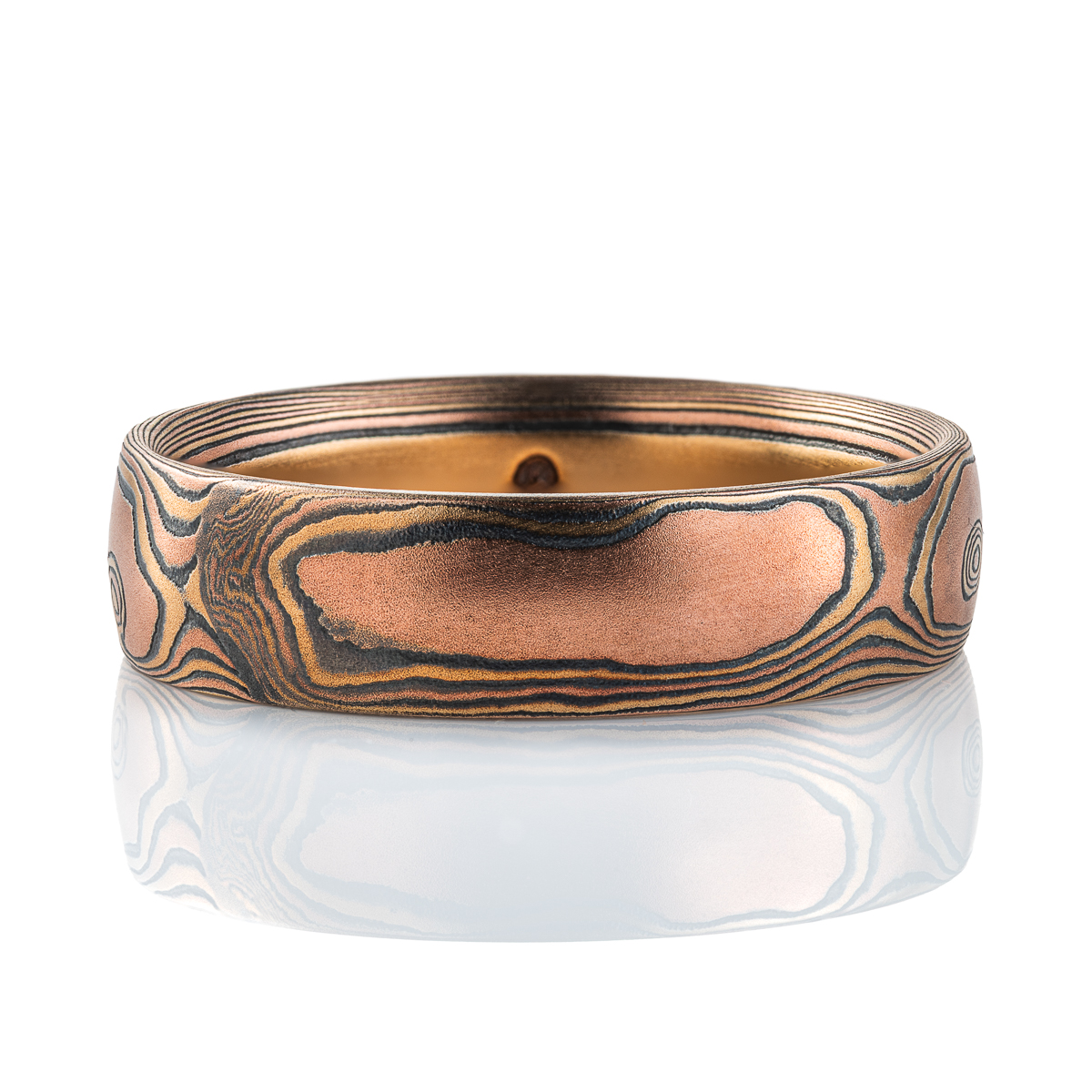 Warm toned mokume gane ring, patterned to look like woodgrain, primarily red gold in color, with yellow gold and oxidized silver (black). .