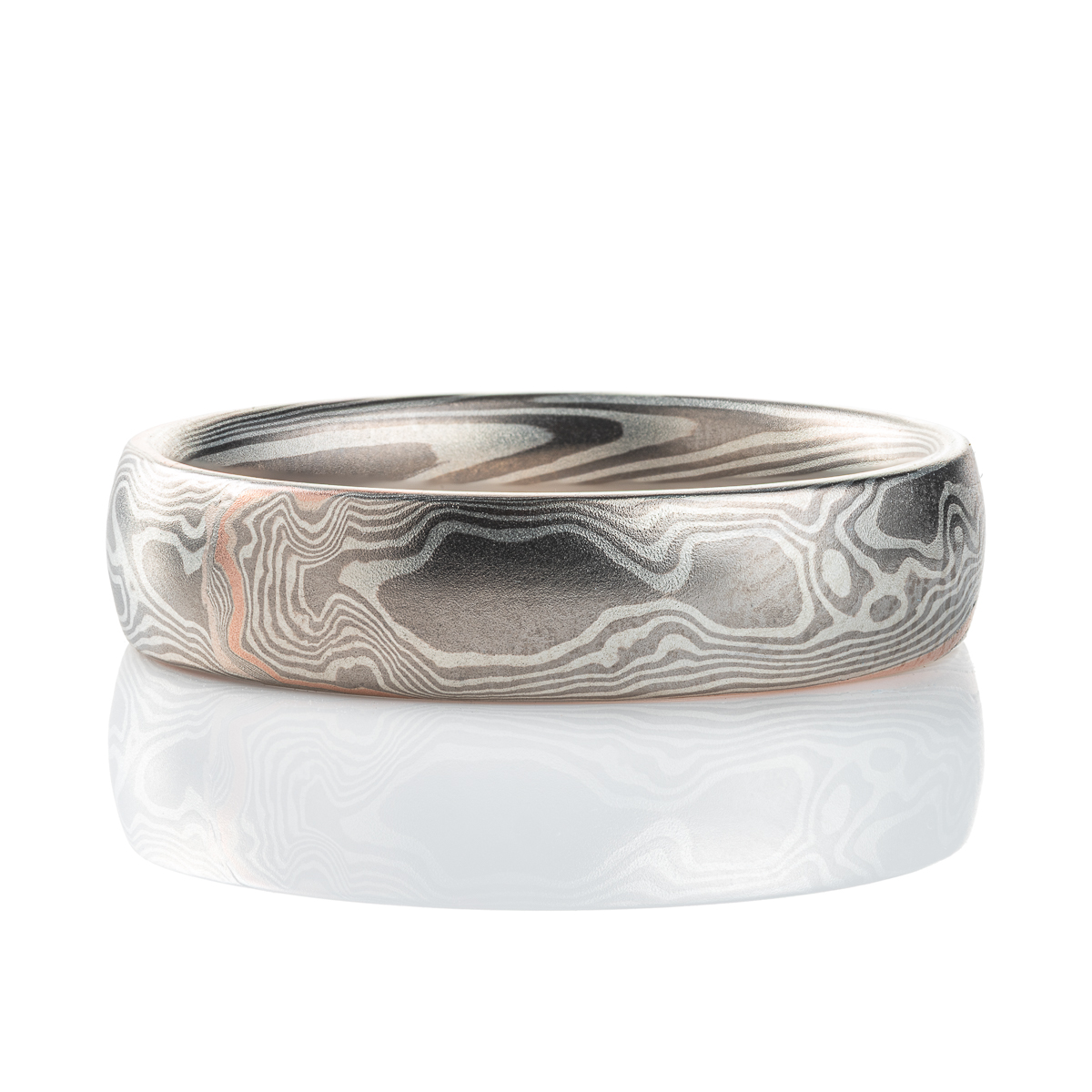 Smooth, domed, slender band patterned in mokume gane twist style, most of the ring is made in silver and palladium, with one stripe of red gold.