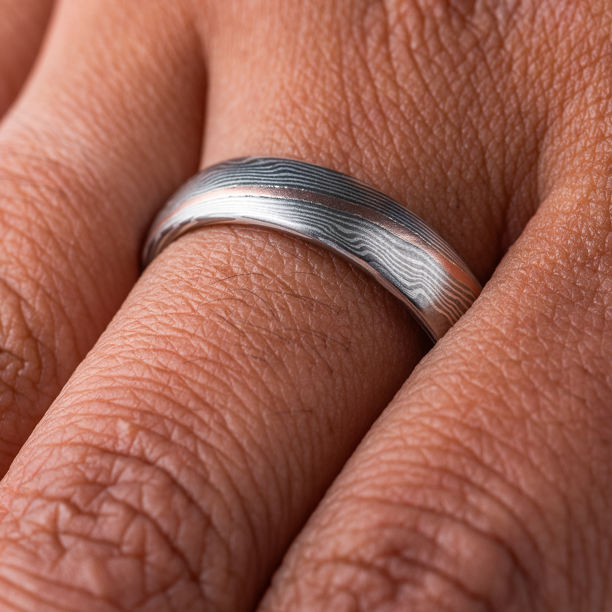Smooth, domed, slender band patterned in mokume gane twist style, most of the ring is made in silver and palladium, with one stripe of red gold.