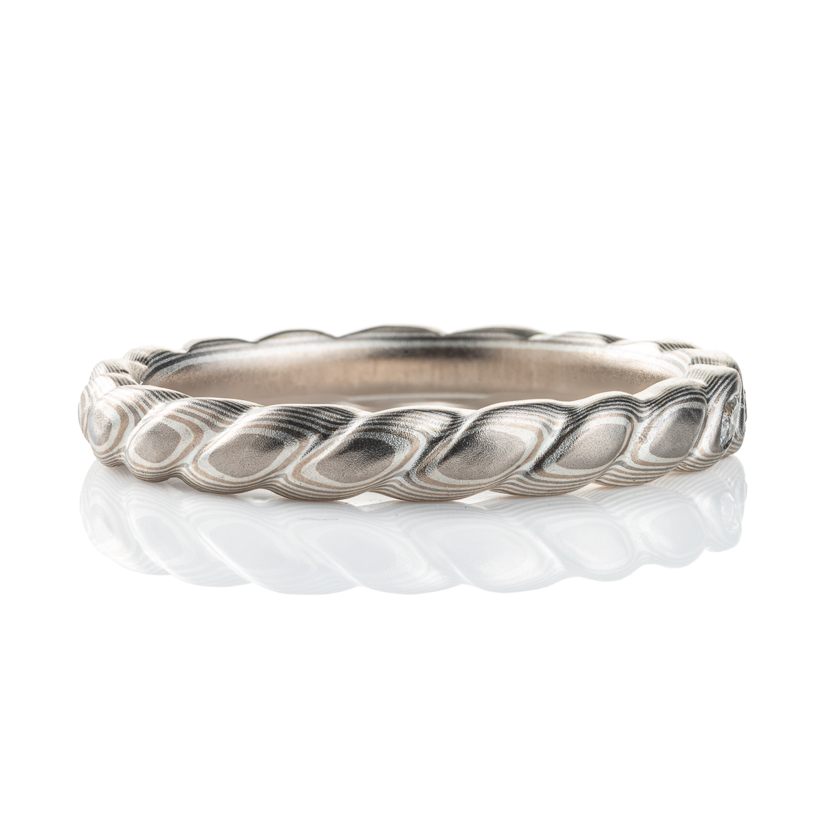 Mokume gane band carved to resemble a twisted rope, with three small flush set marquise shaped diamonds. The ring is overall silver in color palette.