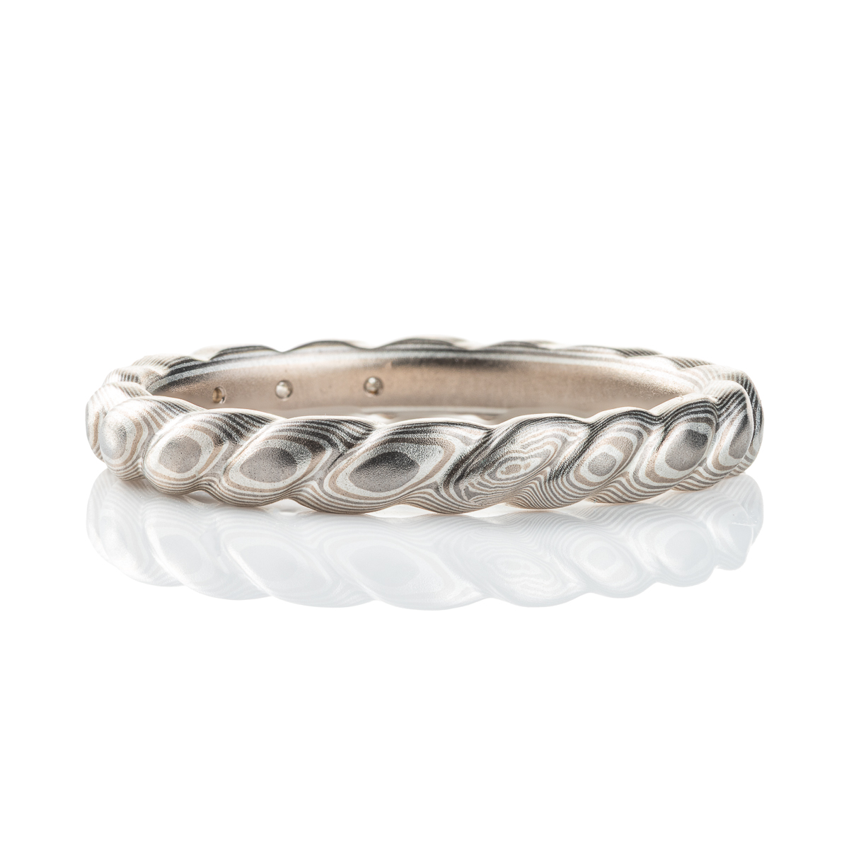 Mokume gane band carved to resemble a twisted rope, with three small flush set marquise shaped diamonds. The ring is overall silver in color palette.