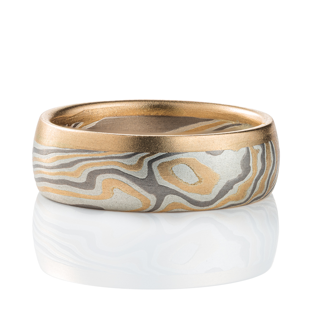 Mokume gane ring made of twisting layers of oxidized silver, palladium and yellow gold, with a solid strip of yellow gold running around one edge.