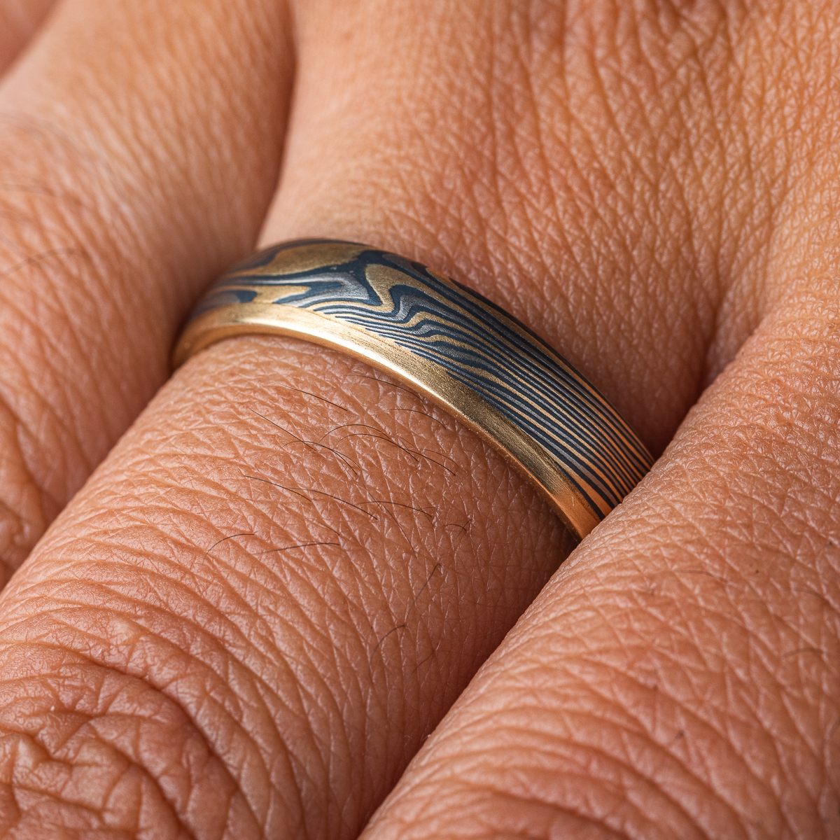 Mokume gane twisted band, with one solid strip of yellow gold running around one edge. The rest of the ring is made of layers of yellow gold, palladium and silver.