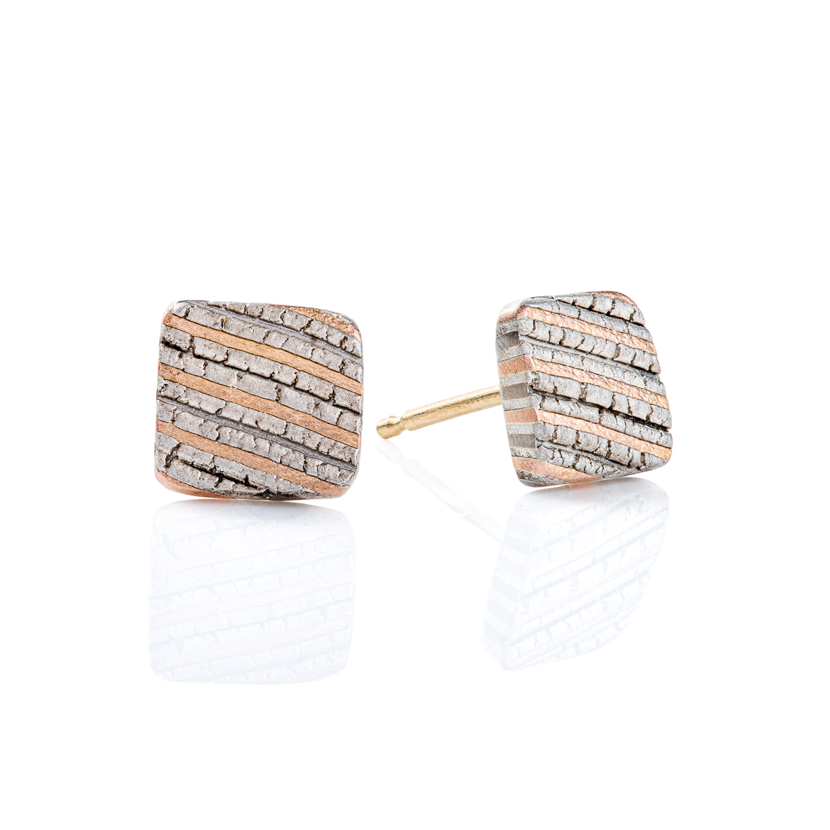 Small flat square stud earrings made with mokume gane, layered stripes of red gold, palladium and silver, with a crackly texture that resembles rock. .