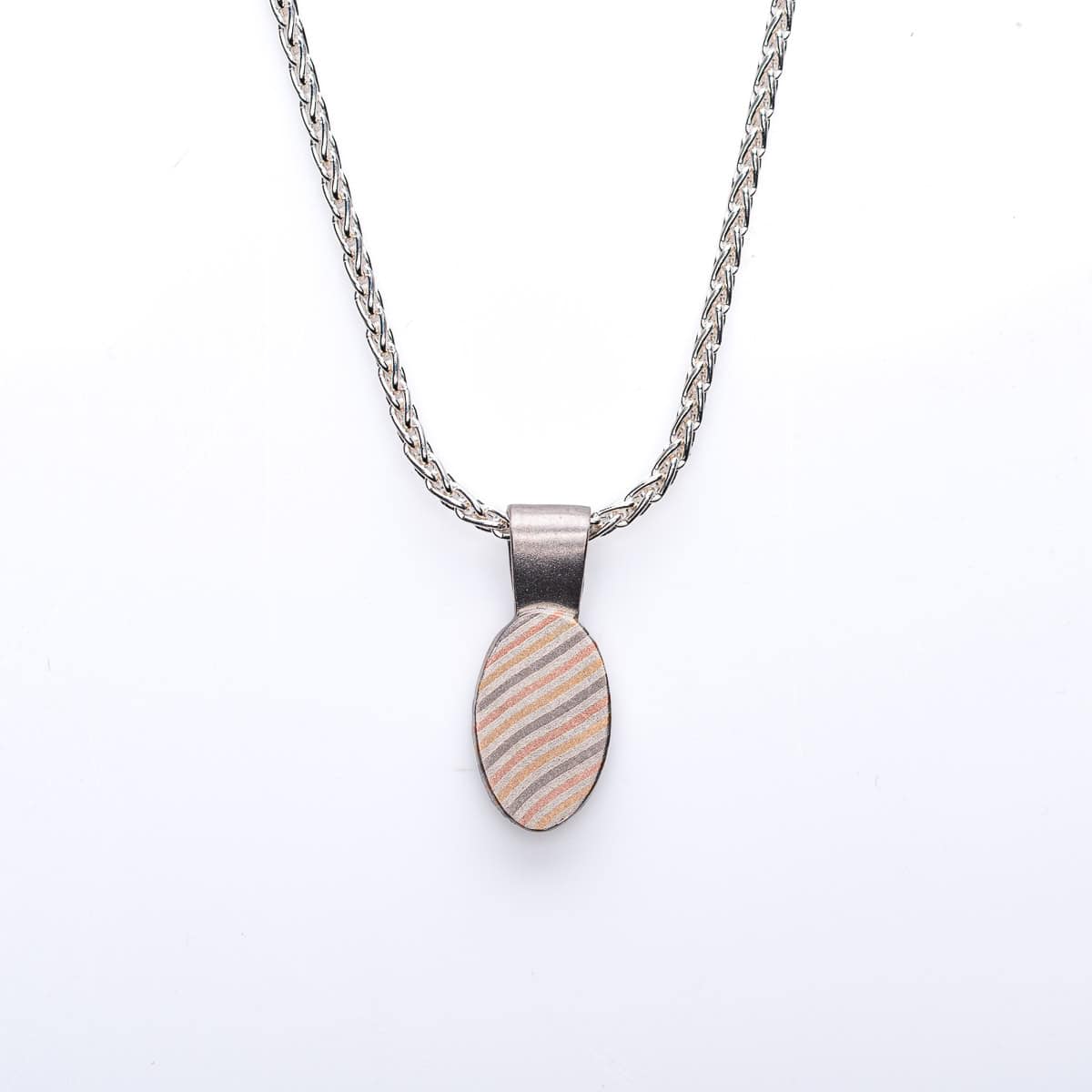 Small mokume gane patterned pendant, oval shaped, hanging on a chain. The pattern resembles stripes running diagonal across the pendant.