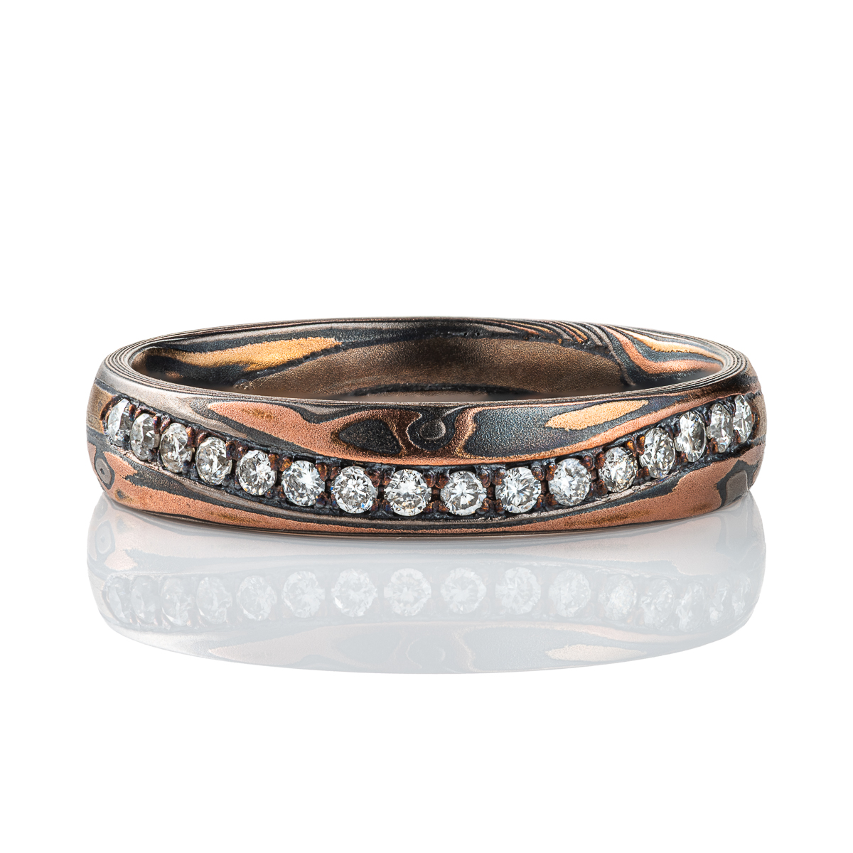 Narrow mokume gane patterned band with undulating line of diamonds set flush into the surface. The band is made of warm toned metals in a woodgrain style pattern.