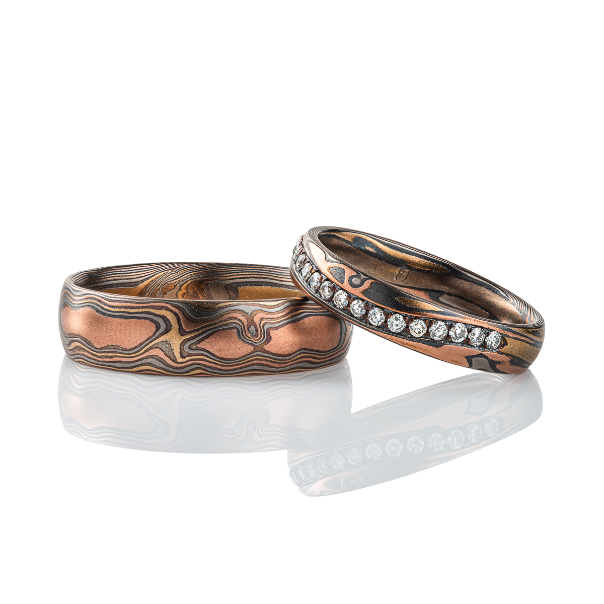 channels set diamonds in a Pair of mokume gane patterned rings made in matching metal combination, with red gold, yellow gold, palladium and oxidized silver. The narrower ring also has a wavy channel set line of small diamonds set into it.