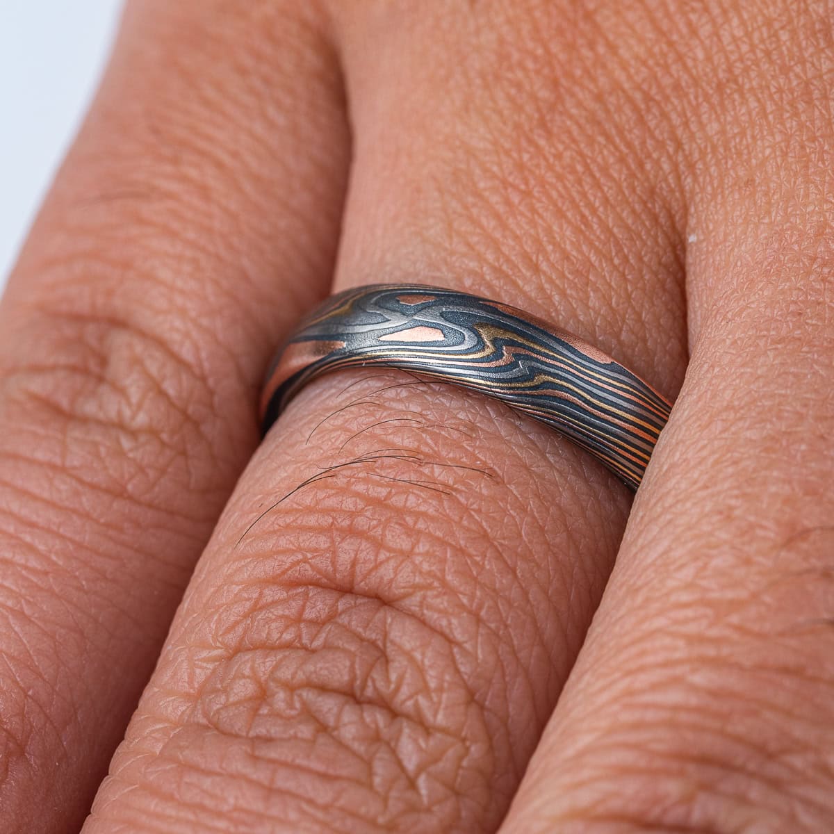 Mokume gane patterned band, made to look like woodgrain, made of layers of red gold, yellow gold, palladium, and oxidized silver.