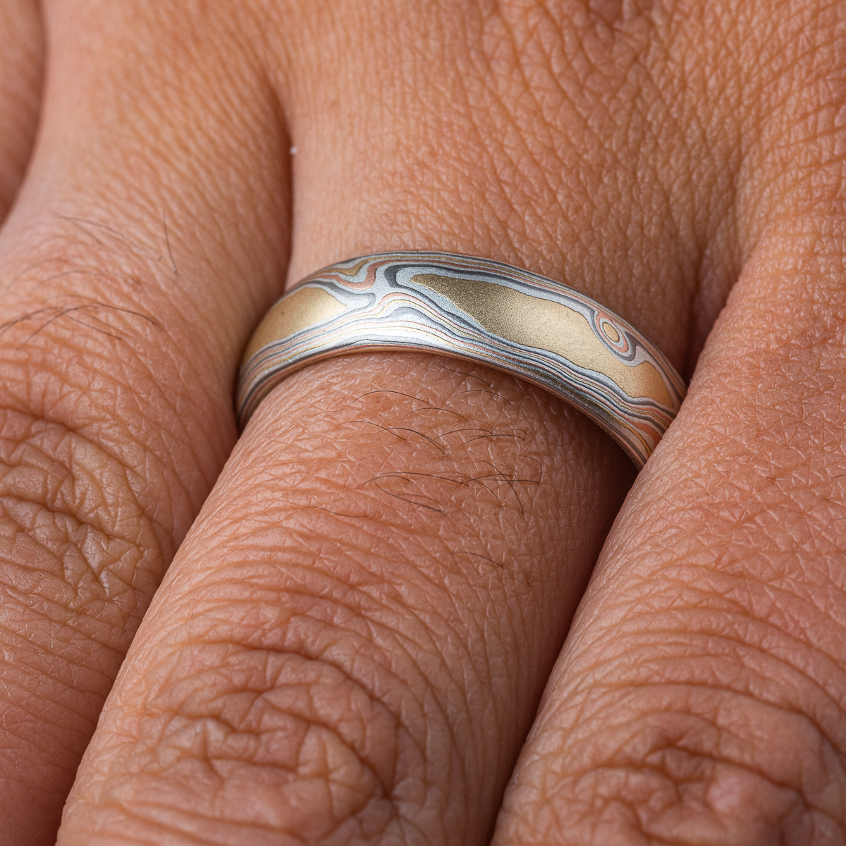 Slim mokume gane patterned band, twisting and organic flowing pattern, made with layers of red gold, yellow gold, palladium, and oxidized silver.