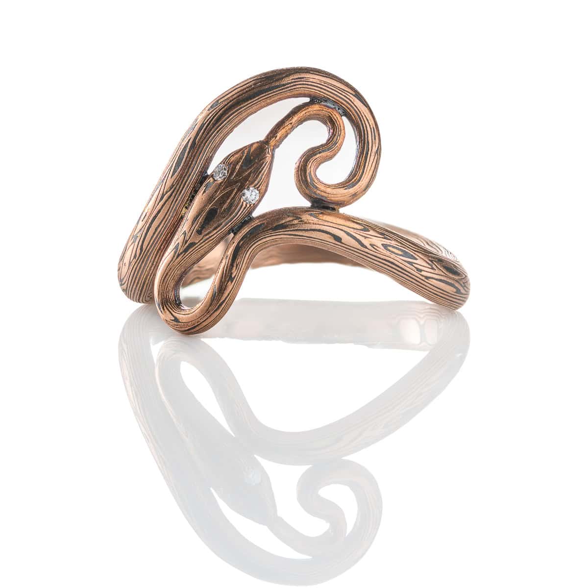 Custom handcrafted and forged mokume gane ring made to look like a snake curling and twisting around the finger. Made with red gold and oxidized silver, with tiny diamonds as eyes.