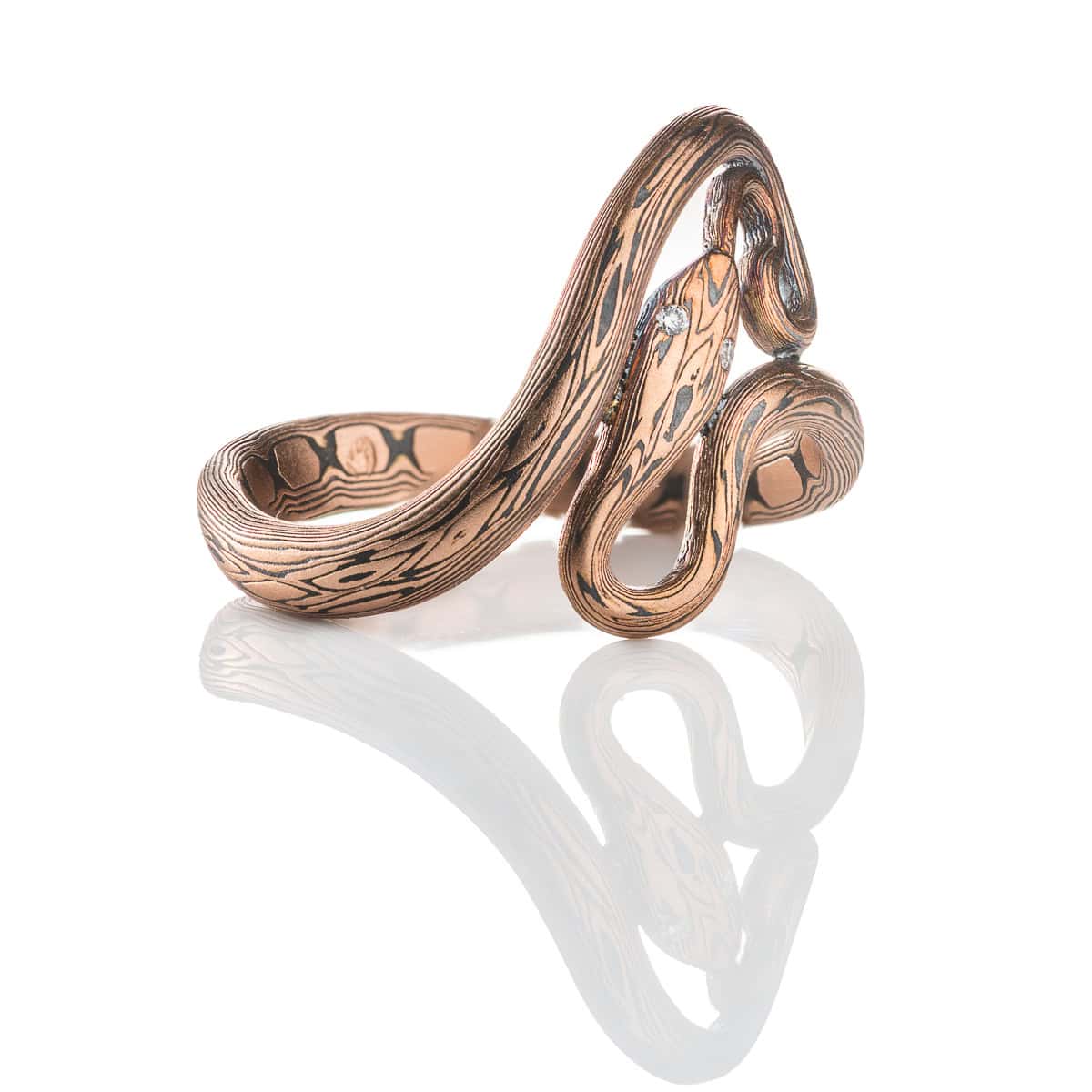 Custom handcrafted and forged mokume gane ring made to look like a snake curling and twisting around the finger. Made with red gold and oxidized silver, with tiny diamonds as eyes.