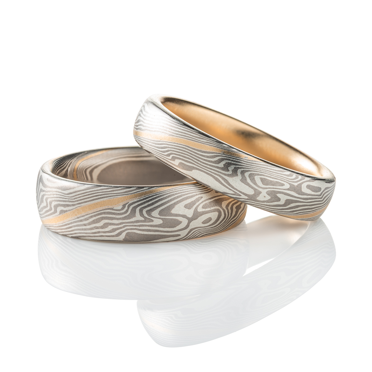 Pair of matching mokume gane woodgrain patterned rings, in a silver and gray palette with a stripe of yellow gold. The smaller ring has also been lined with yellow gold.