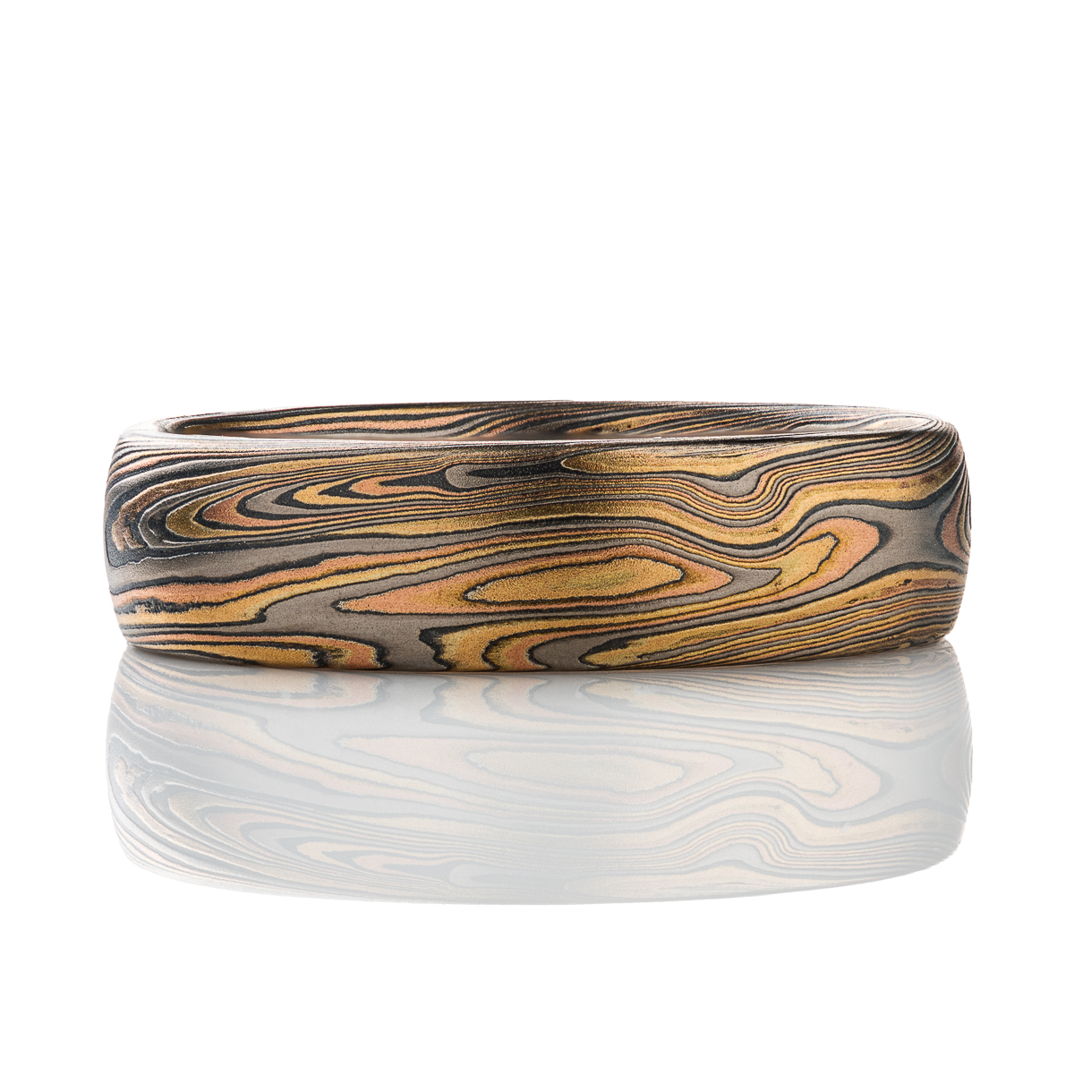 Patterned mokume gane men’s ring, made with red gold, yellow gold, palladium and oxidized silver. The pattern is organic feeling, swirling, sweeping lines.