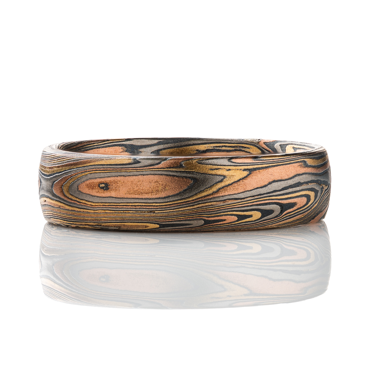 Patterned mokume gane men’s ring, made with red gold, yellow gold, palladium and oxidized silver. The pattern is organic feeling, swirling, sweeping lines.