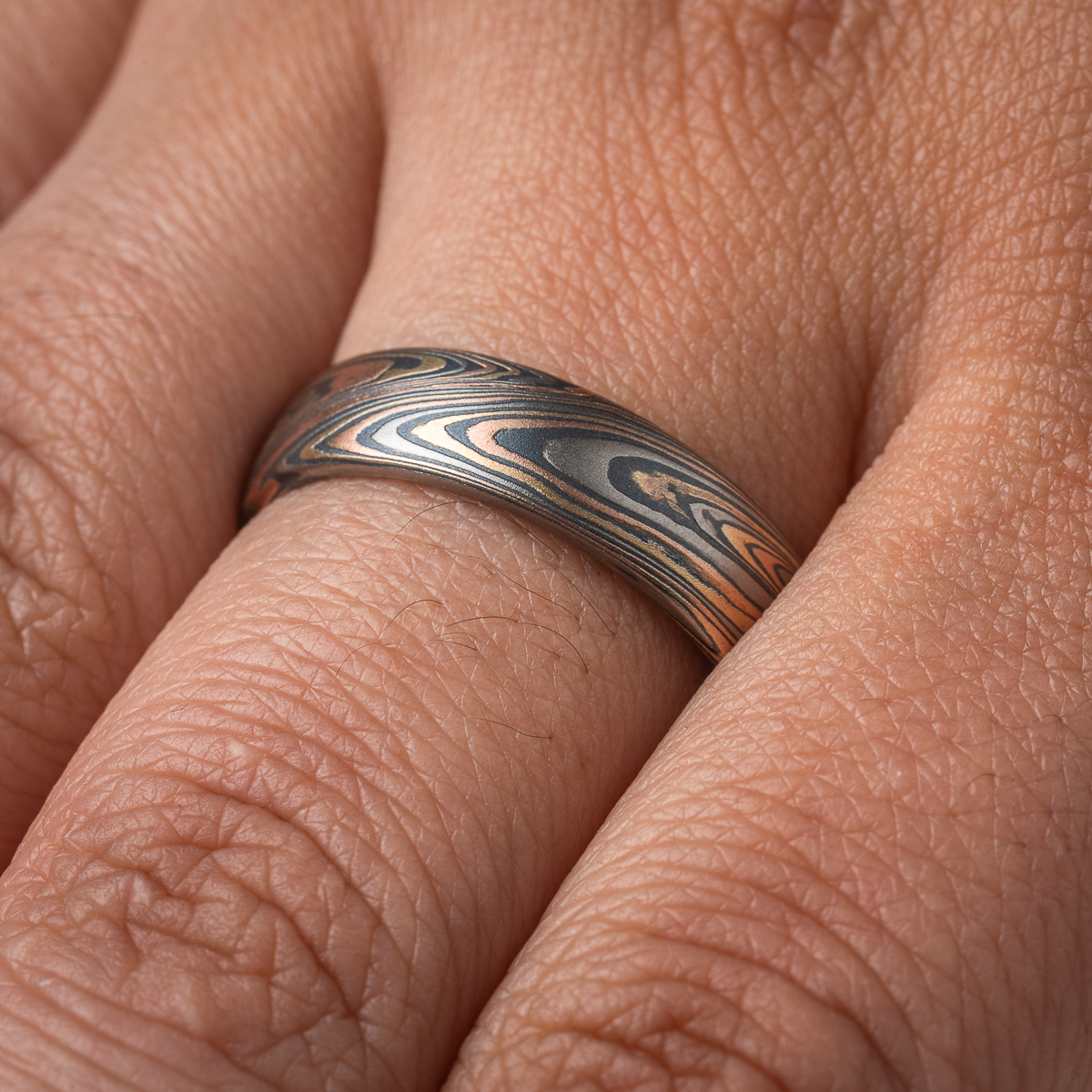 Patterned mokume gane men’s ring, made with red gold, yellow gold, palladium and oxidized silver. The pattern is organic feeling, swirling, sweeping lines.