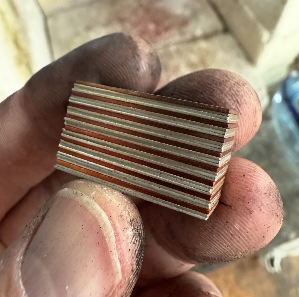 Hand holding a stack of thin layers of metal fused together to make a billet, used to make mokume gane.