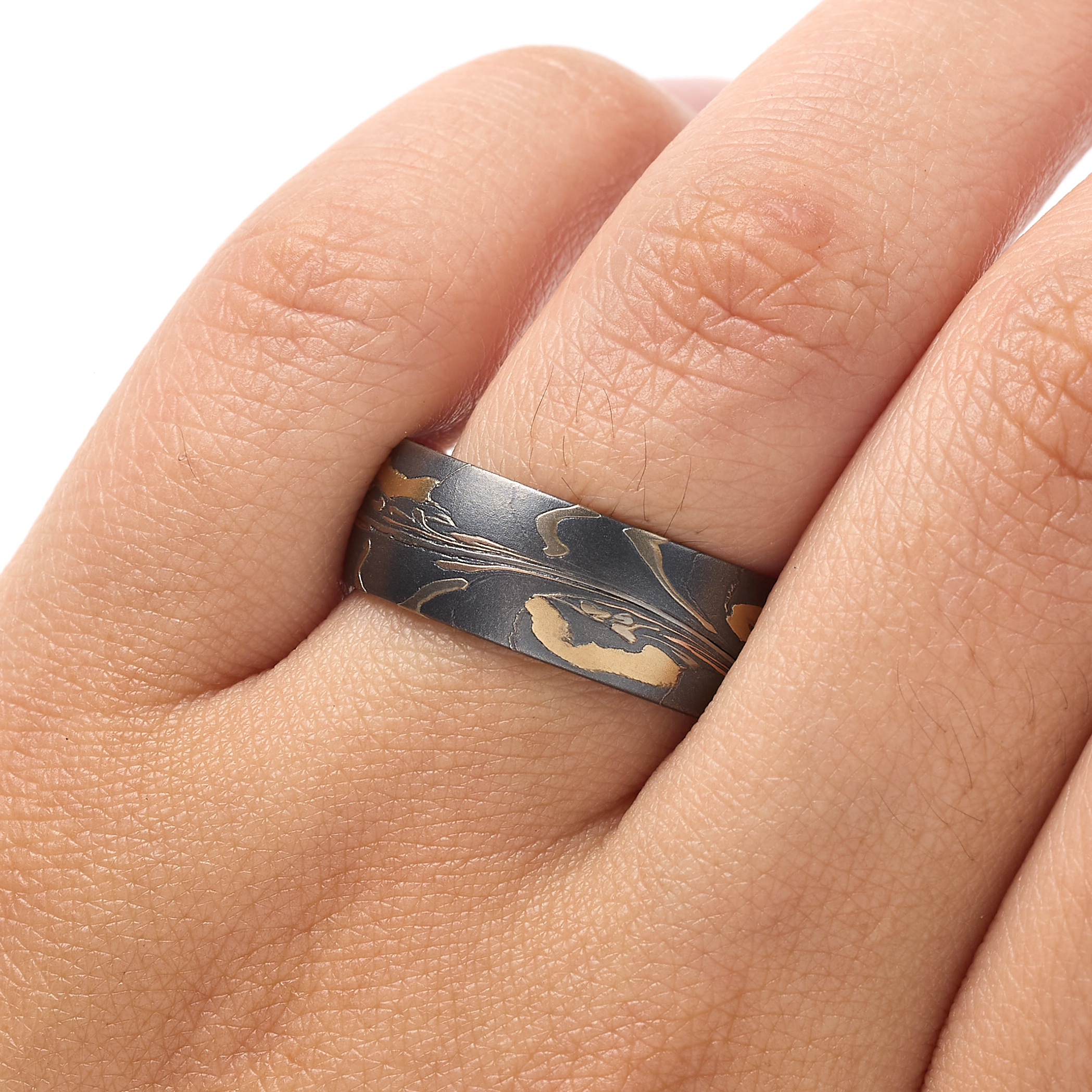 Arn Krebs mokume gane mens ring made in an organic unique pattern, with layers of yellow gold, red gold, palladium, and silver that's been oxidized. The pattern resembles pressed flower petals on a dark backdrop.