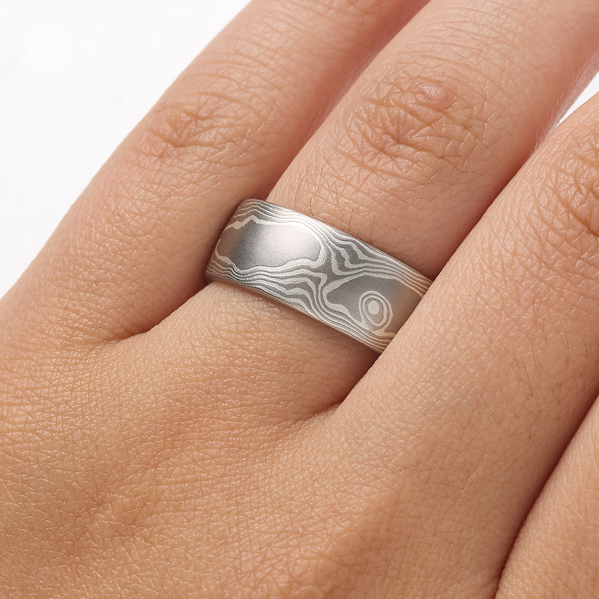 Mokume gane ring patterned in a classic woodgrain style, made with layers of palladium and silver, lightly etched for a slight texture, wide to suit a men's style, and with a low dome profile.